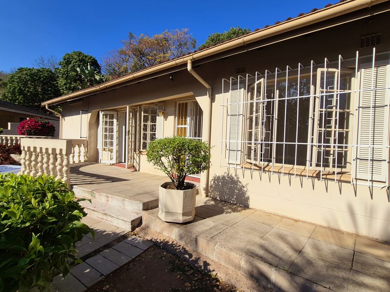 Rear exterior view of the house featuring a tiled patio area, security bars on windows, and a balustrade overlooking the garden.