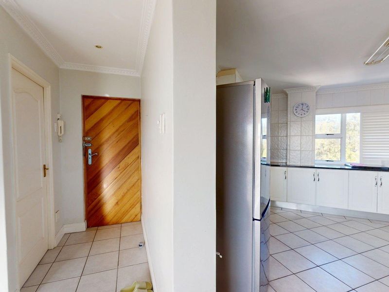 Open plan apartment layout featuring a tiled entrance hallway leading into a functional kitchen with built-in cabinetry and stone countertops.