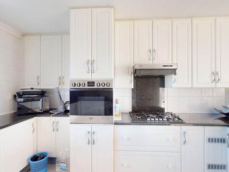 A well-maintained kitchen featuring white cabinetry, granite countertops, a built-in oven, and a gas hob with an extractor fan.