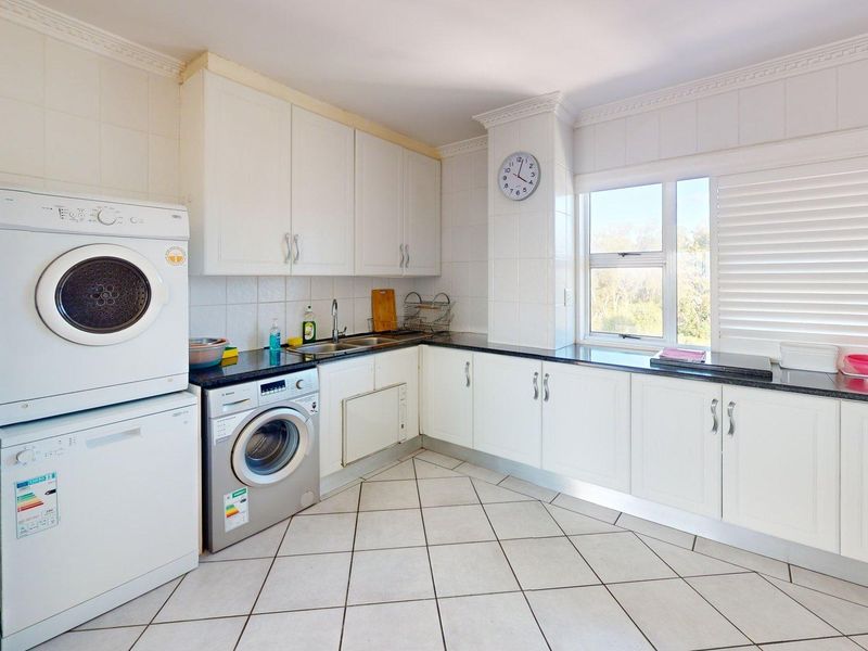 A functional kitchen featuring white cabinetry, granite countertops, tiled flooring, and integrated laundry appliances, offering a clean and practical workspace.