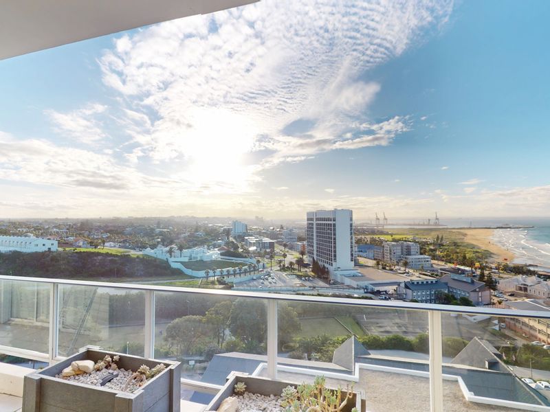 A spacious balcony featuring a modern glass balustrade, offering expansive panoramic views of the coastline and surrounding urban landscape.