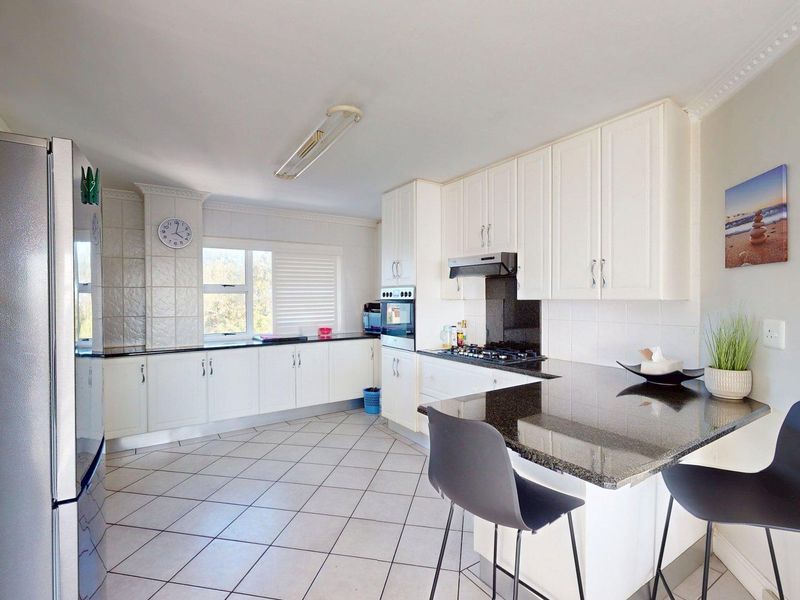 A functional kitchen featuring white cabinetry, dark granite countertops, a breakfast bar, and tiled flooring, offering a clean and practical cooking space.