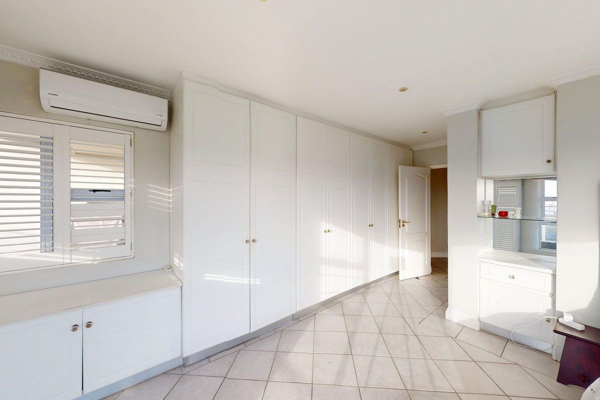 Spacious bedroom featuring extensive built-in cabinetry, plantation shutters, tiled flooring, and a wall-mounted air conditioning unit.
