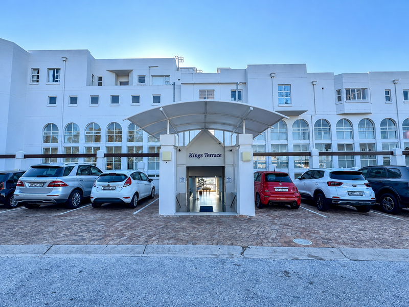Front elevation of Kings Terrace apartment complex featuring a paved parking area and a covered pedestrian entrance canopy.