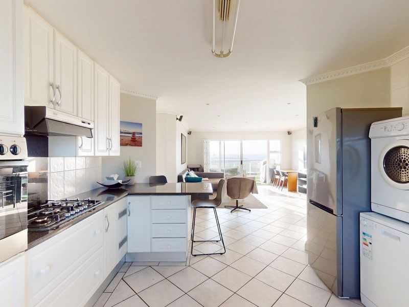 Open-plan kitchen and living area featuring tiled floors, white cabinetry, built-in appliances, and sliding doors leading to an outdoor space.