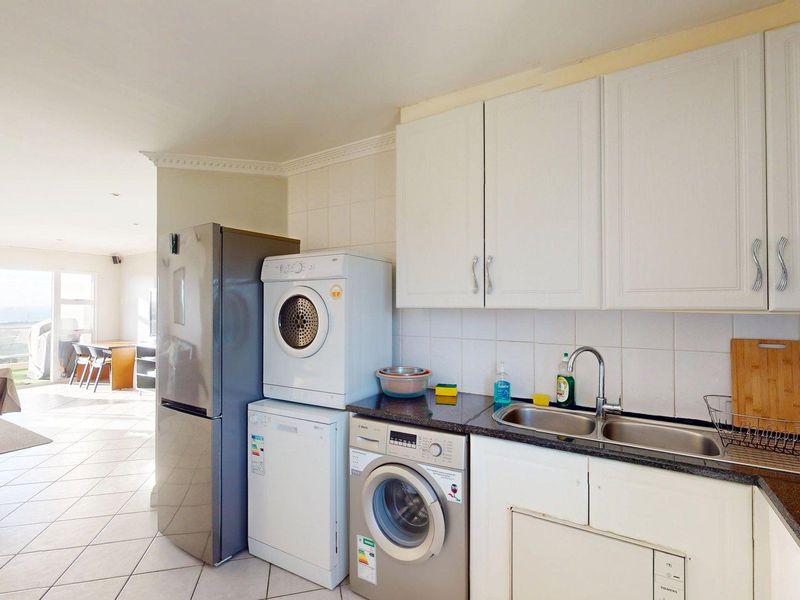 Compact kitchen featuring white cabinetry, granite countertops, a double bowl sink, and tiled backsplash, seamlessly flowing into the adjacent living area.