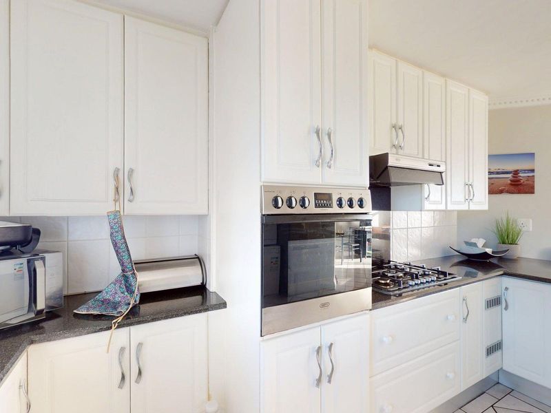 A well-maintained kitchen featuring white cabinetry, granite countertops, a built-in oven, and a gas hob with an extractor fan.