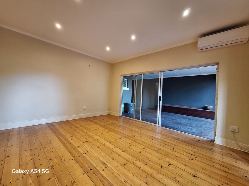 Spacious living area featuring polished timber flooring, recessed downlighting, a wall-mounted air conditioning unit, and sliding glass doors leading to an adjacent room.