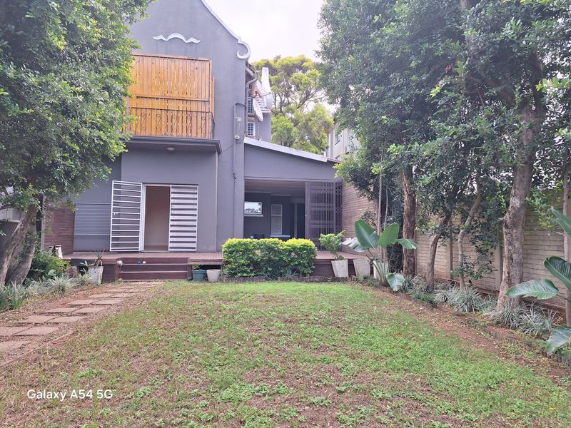 Rear view of the property featuring a timber deck, security gates, and a private garden area with established trees and boundary walling.
