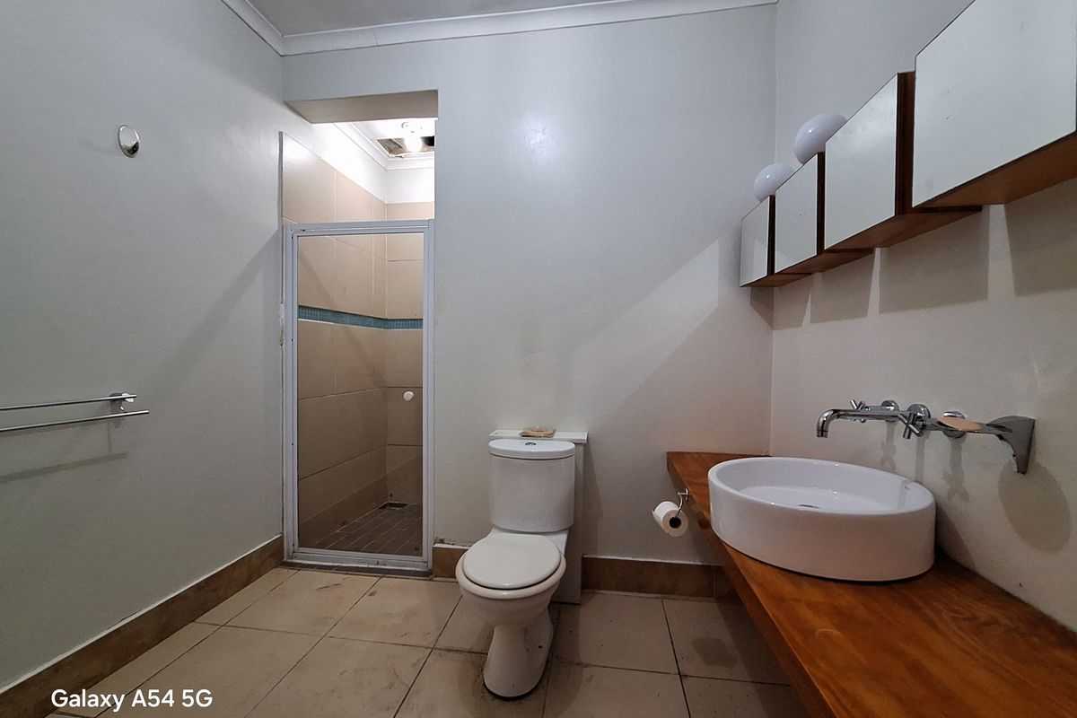 A functional bathroom featuring a walk-in shower, a modern vessel sink on a timber vanity, and wall-mounted storage cabinets.