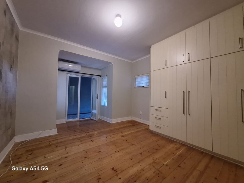 Spacious bedroom featuring polished timber flooring, extensive built-in cabinetry, and direct access to an outdoor area via sliding glass doors.