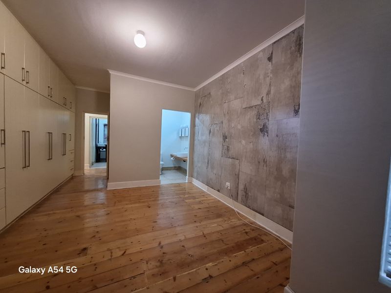 Spacious bedroom featuring polished hardwood flooring, extensive built-in cabinetry, and a decorative feature wall, with direct access to an en-suite bathroom.