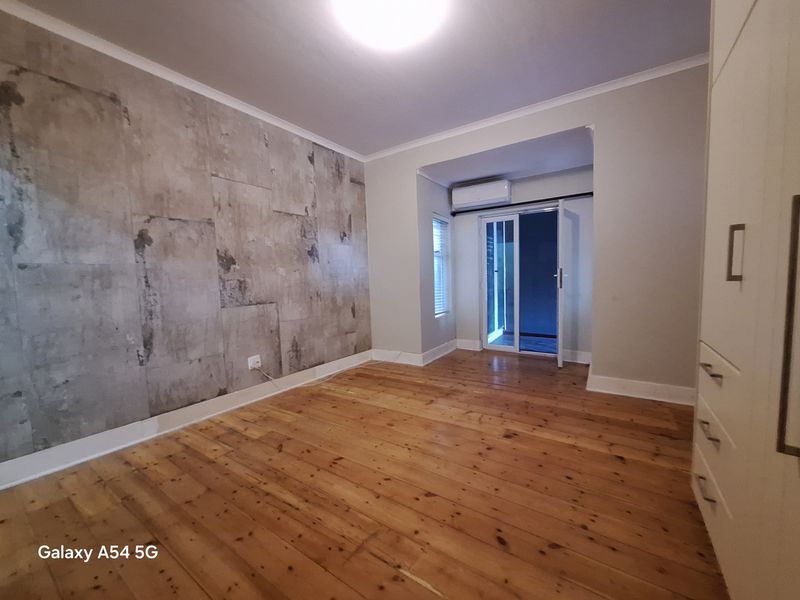 A spacious bedroom featuring polished timber flooring, a built-in wardrobe, a feature wall, and direct access to an outdoor area via sliding glass doors.
