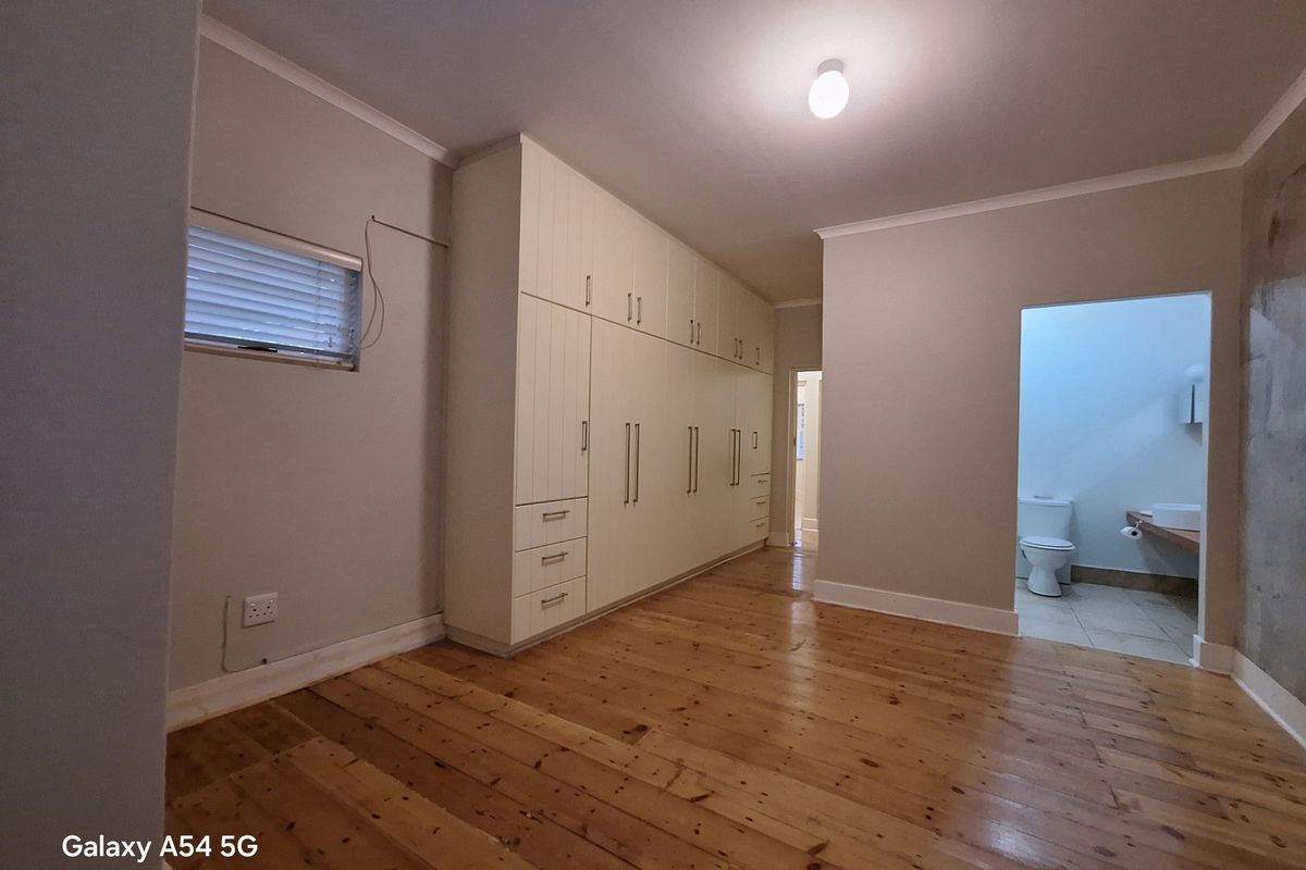 Spacious bedroom featuring polished timber flooring, extensive built-in cabinetry, and an en-suite bathroom access.
