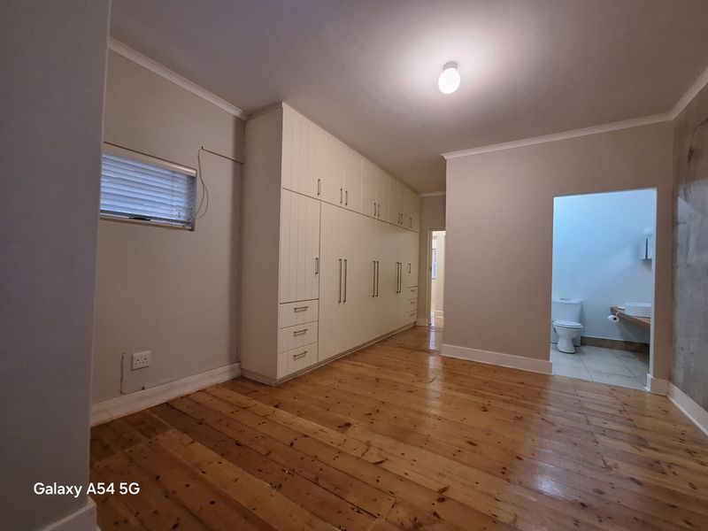 Spacious bedroom featuring polished timber flooring, extensive built-in cabinetry, and an en-suite bathroom access.