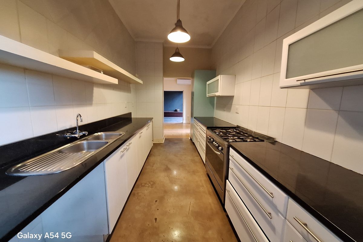 A galley-style kitchen featuring black granite countertops, a gas stove, double sink, and polished concrete floors, offering a functional and clean workspace.