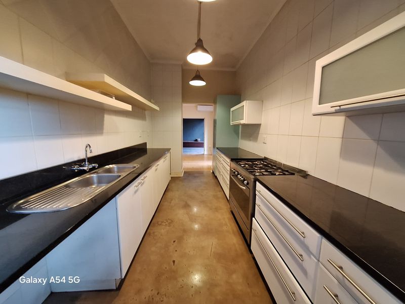 A galley-style kitchen featuring black granite countertops, a gas stove, double sink, and polished concrete floors, offering a functional and clean workspace.