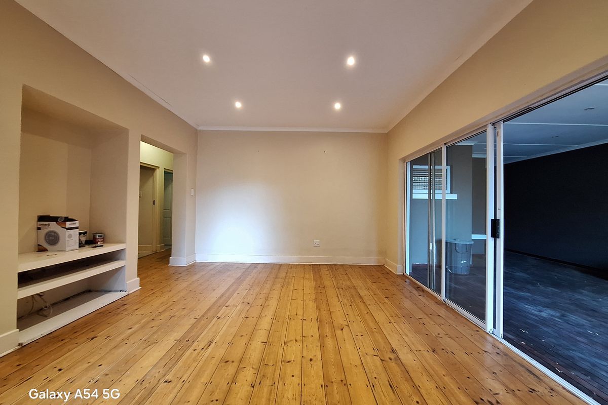 Spacious living area featuring polished timber flooring, recessed downlights, and a built-in shelving unit, with large sliding glass doors opening to an outdoor space.