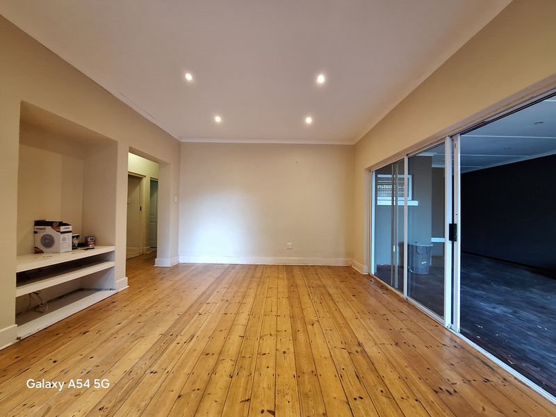 Spacious living area featuring polished timber flooring, recessed downlights, and a built-in shelving unit, with large sliding glass doors opening to an outdoor space.