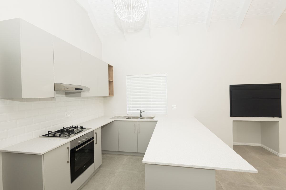 Modern kitchen featuring light grey cabinetry, quartz countertops, gas cooktop, built-in oven, and a vaulted ceiling with an integrated fireplace.