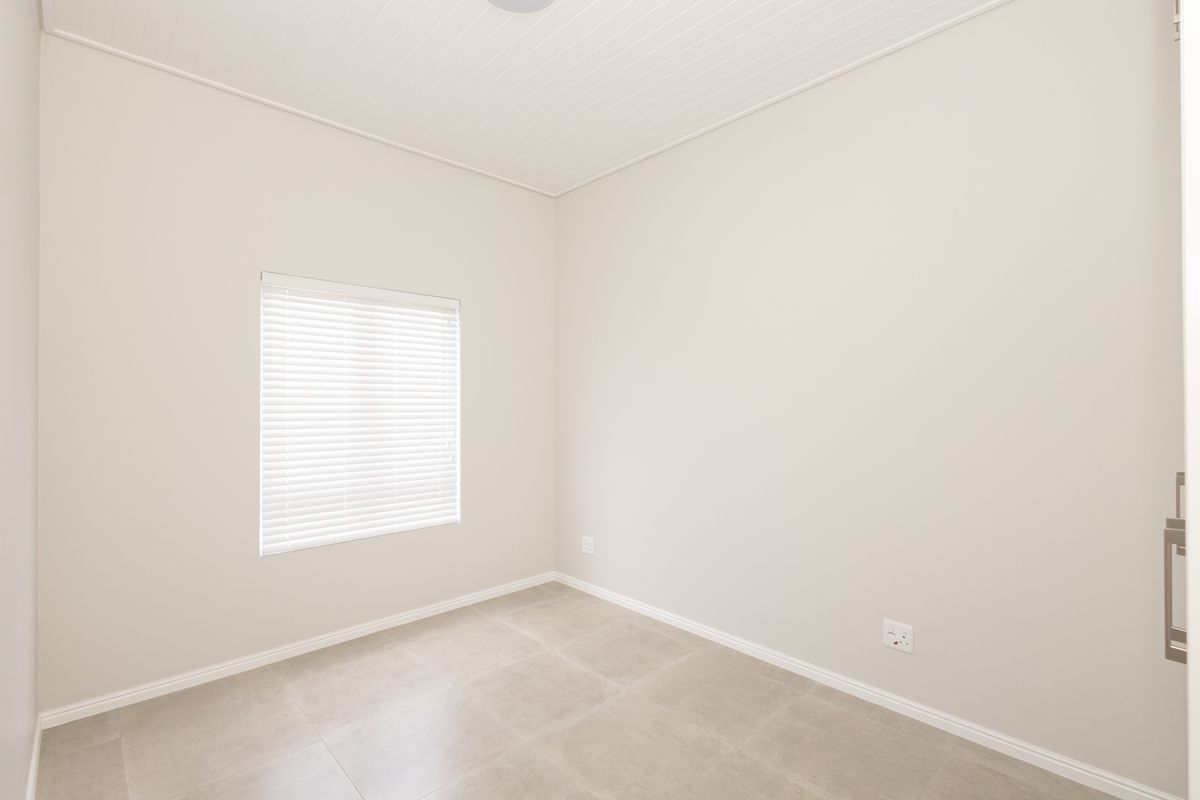 A clean, neutral, and empty bedroom featuring tiled flooring, a tongue and groove ceiling, and a window fitted with venetian blinds.