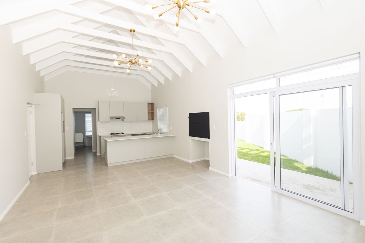 Spacious open-plan living area featuring a modern kitchen with island, vaulted ceilings with exposed rafters, and large sliding doors leading to the garden.