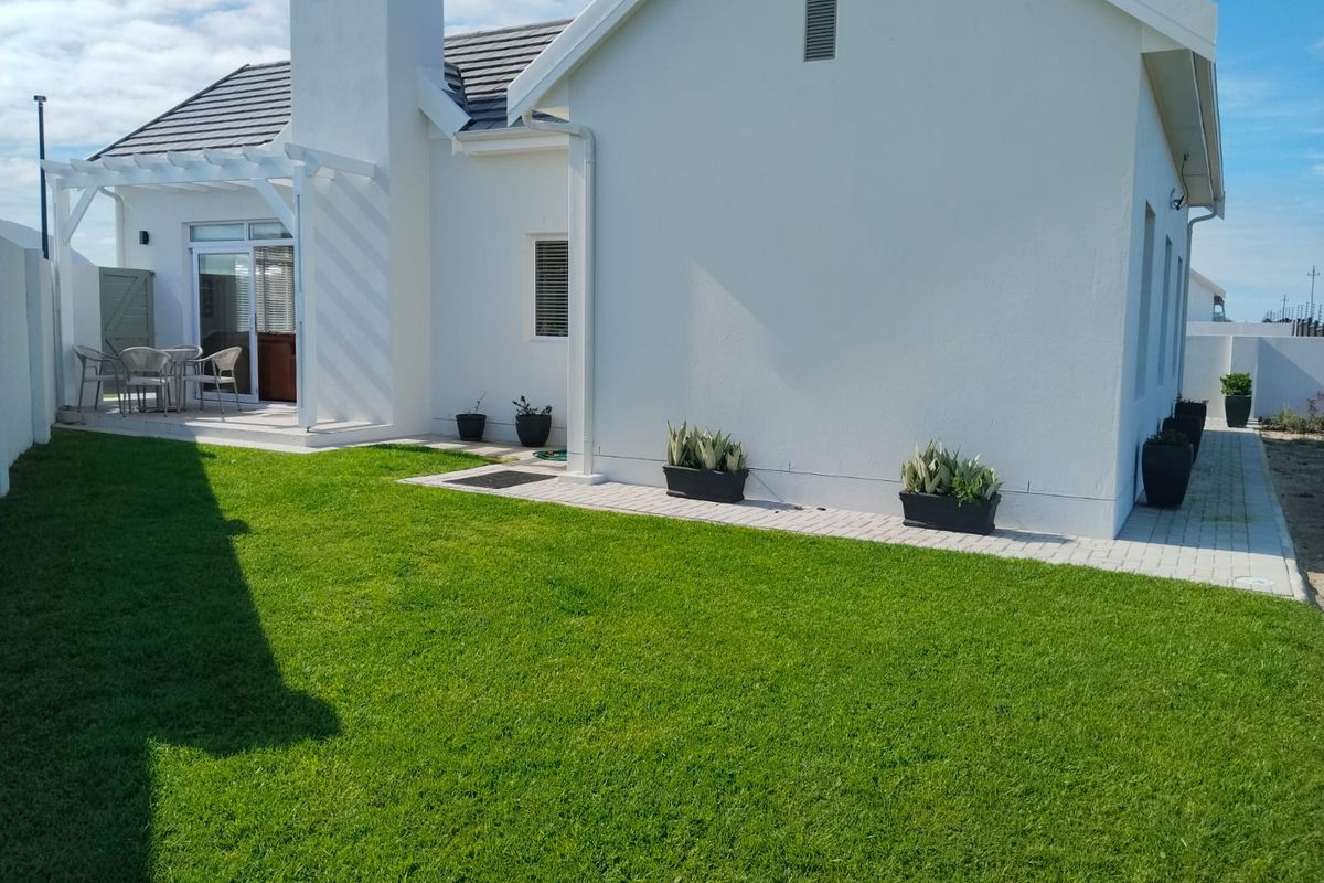 A well-maintained rear exterior view featuring a manicured lawn, paved walkway, and a covered patio area with a chimney.