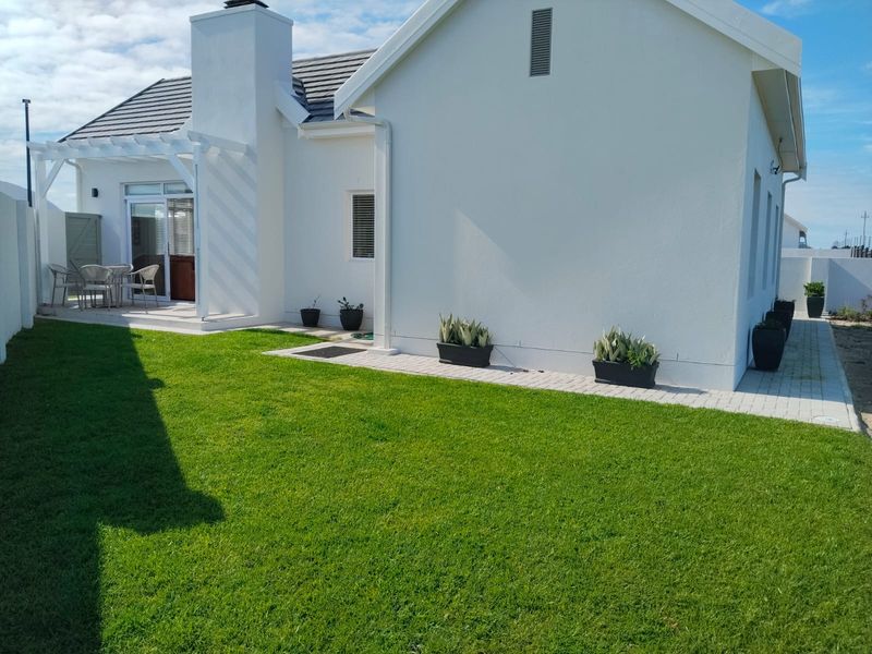 A well-maintained rear exterior view featuring a manicured lawn, paved walkway, and a covered patio area with a chimney.