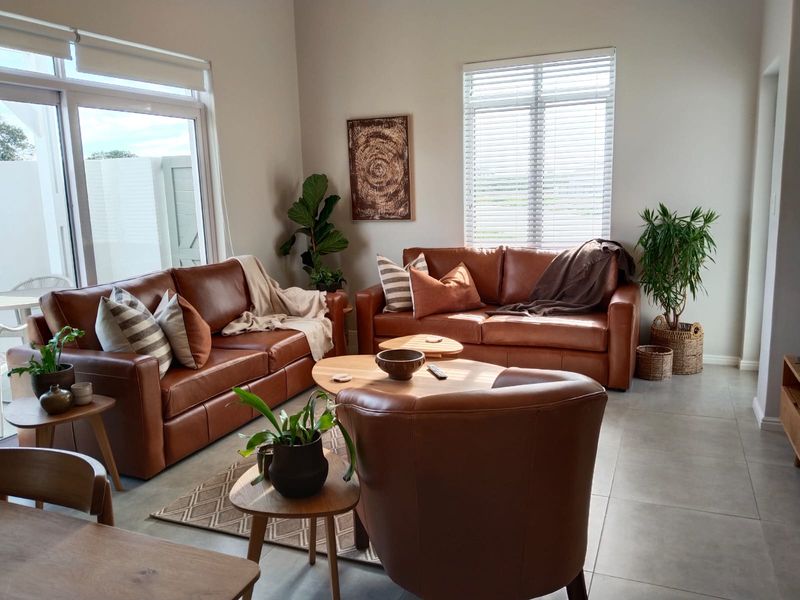 A bright and well-maintained living room featuring large windows with blinds, tiled flooring, and a sliding glass door leading to an outdoor area.