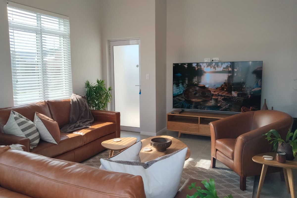 A bright and well-maintained living room featuring tiled flooring, a frosted glass door, and venetian blinds, offering a comfortable and inviting atmosphere.