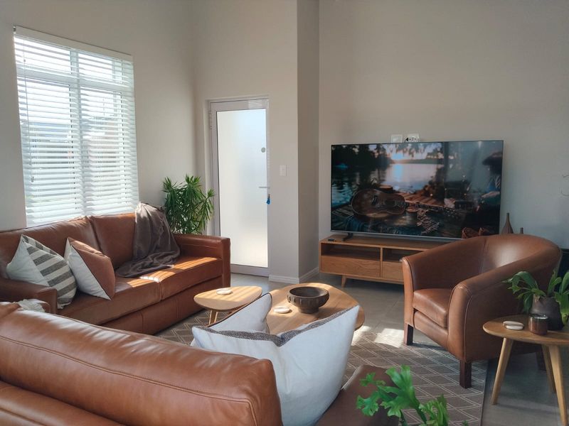 A bright and well-maintained living room featuring tiled flooring, a frosted glass door, and venetian blinds, offering a comfortable and inviting atmosphere.