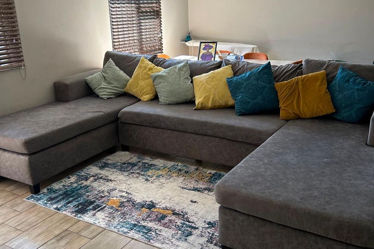 A comfortable living room featuring wood-look tiled flooring, neutral wall tones, and venetian blinds, providing a functional and well-maintained space.