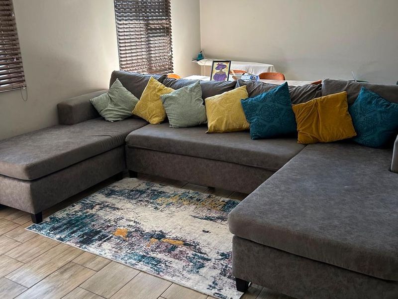 A comfortable living room featuring wood-look tiled flooring, neutral wall tones, and venetian blinds, providing a functional and well-maintained space.