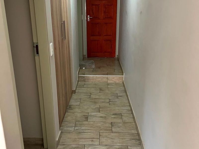 A clean, well-maintained hallway featuring wood-look floor tiles, built-in storage cabinetry, and a solid timber door.