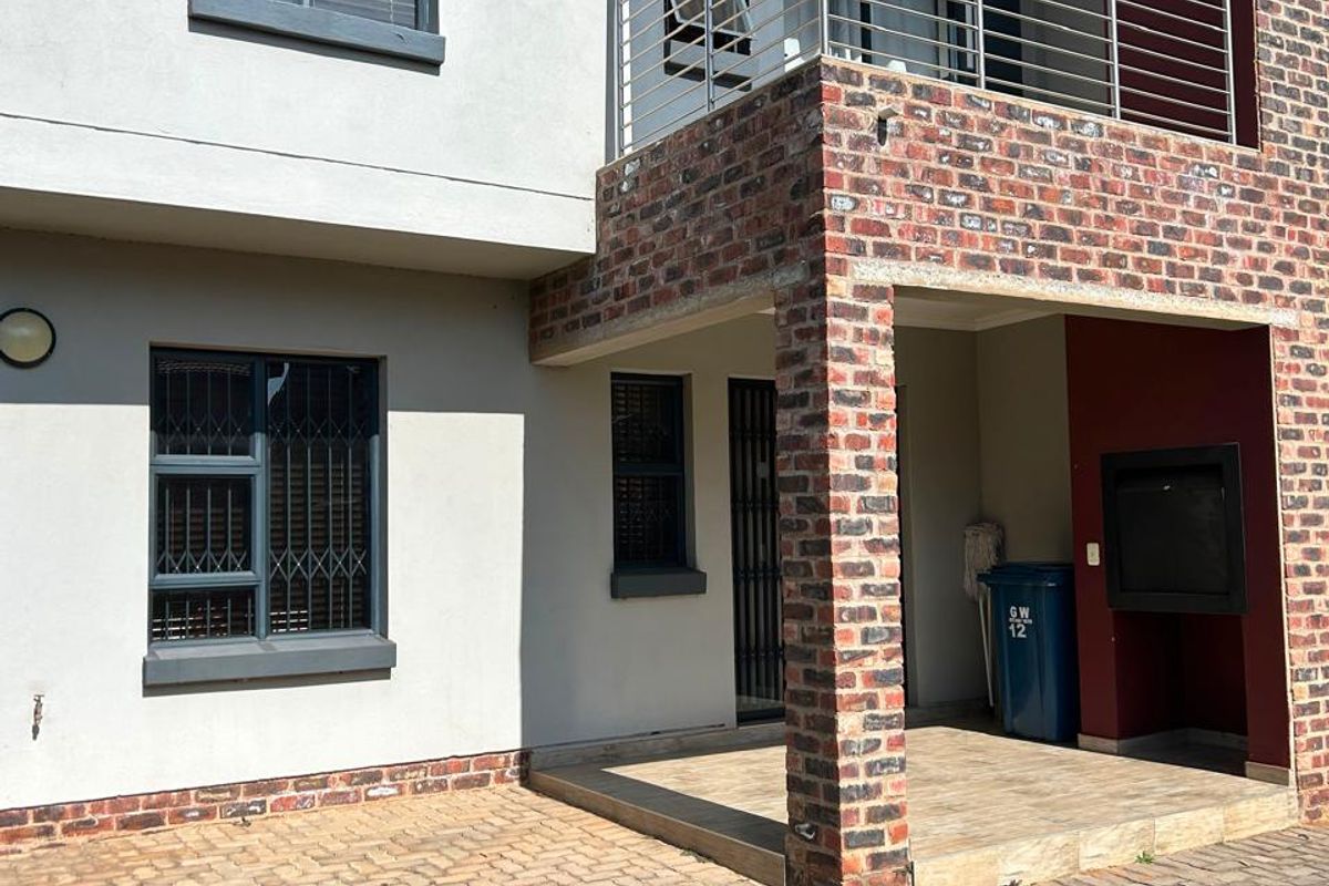 Rear view of the townhouse featuring a paved patio, built-in braai area, and an upper-level balcony with modern stainless steel railings.