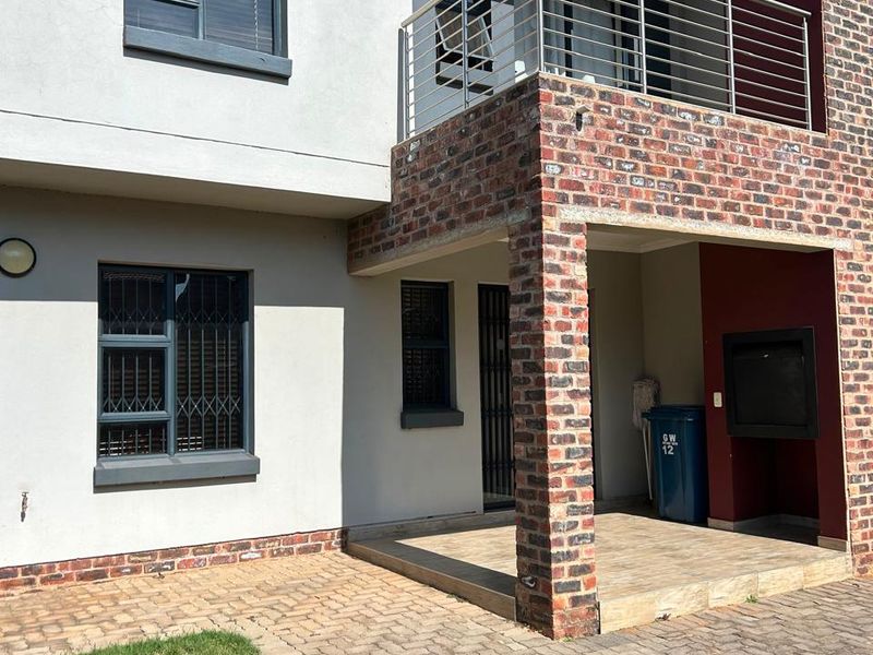 Rear view of the townhouse featuring a paved patio, built-in braai area, and an upper-level balcony with modern stainless steel railings.
