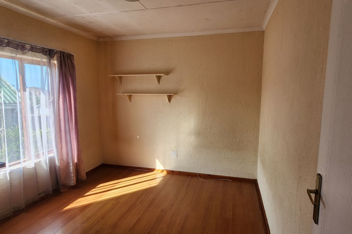 An empty bedroom featuring laminate flooring, built-in wall shelving, and natural light from a large window.