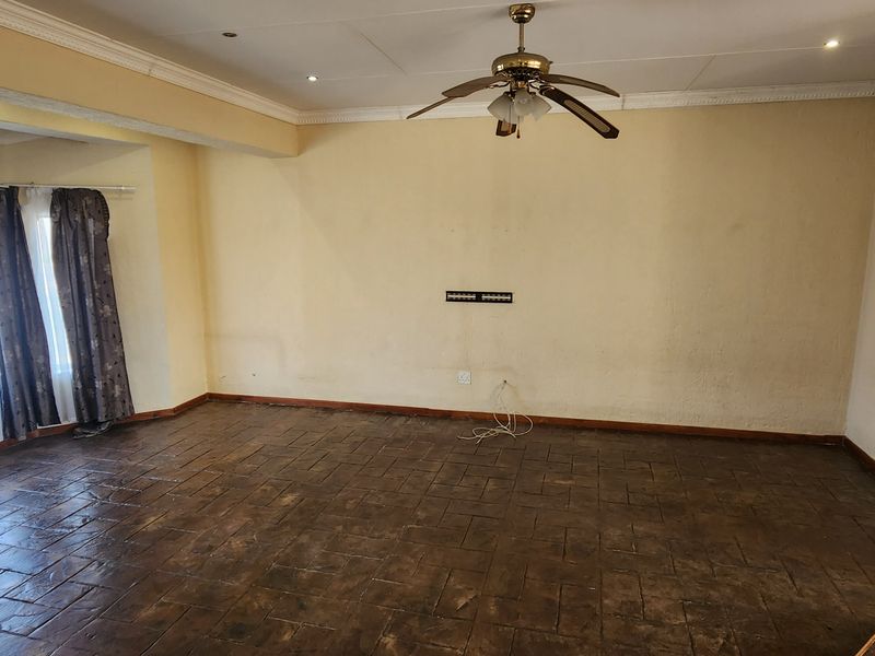 An empty living room featuring tiled flooring, crown molding, and a ceiling fan, requiring cosmetic updates to the wall finishes.