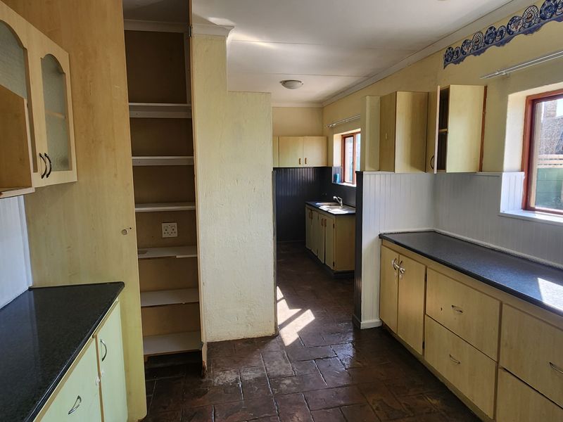 A dated kitchen featuring extensive laminate cabinetry, dark countertops, a double sink, and tiled flooring, offering significant potential for a modern renovation.