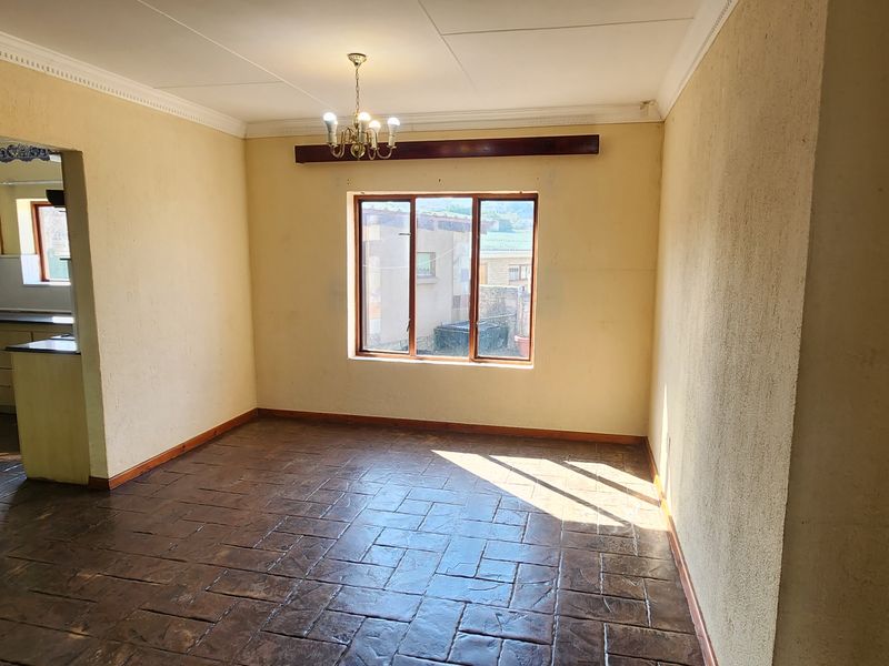 An empty open-plan living area featuring tiled flooring, coved ceilings, and a central chandelier, offering a blank canvas for renovation.