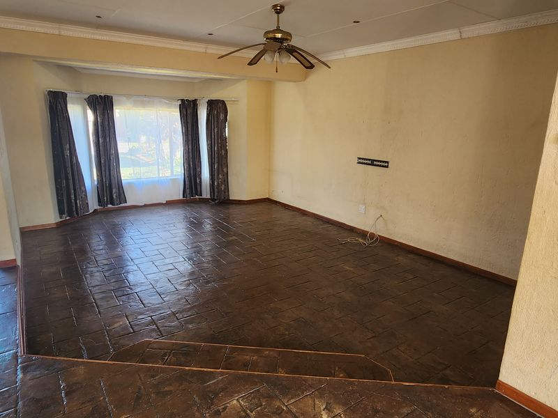 An empty, sunken living room featuring dark tiled flooring, a ceiling fan, and coved ceilings, offering a blank canvas for renovation.