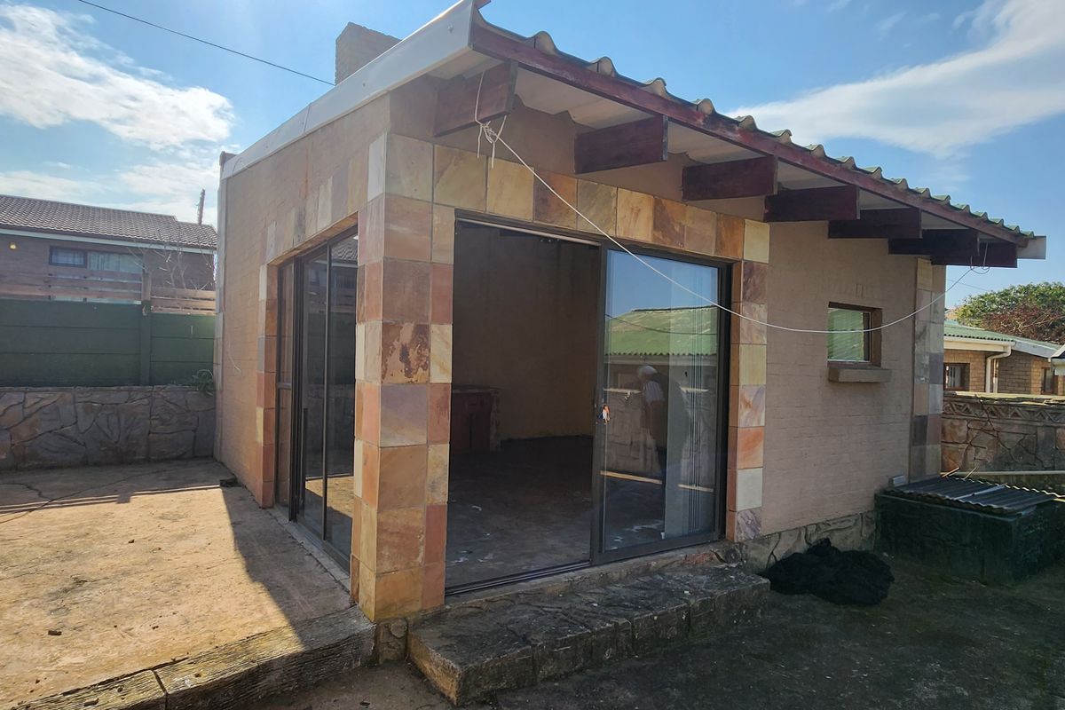 Rear view of a detached structure featuring stone tile accents, sliding glass doors, and an attached concrete patio area.