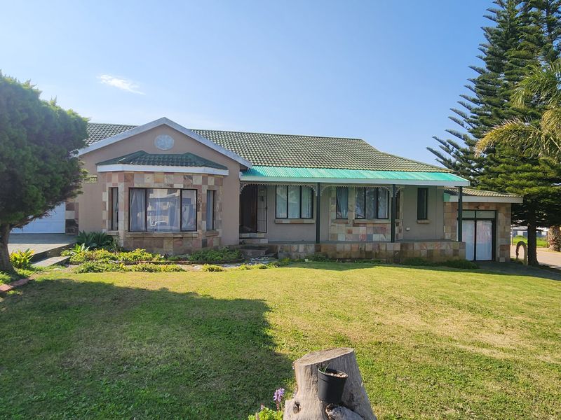 Front elevation of a single-story house featuring stone cladding, a tiled roof, a covered veranda, and a well-maintained front garden with a paved driveway.