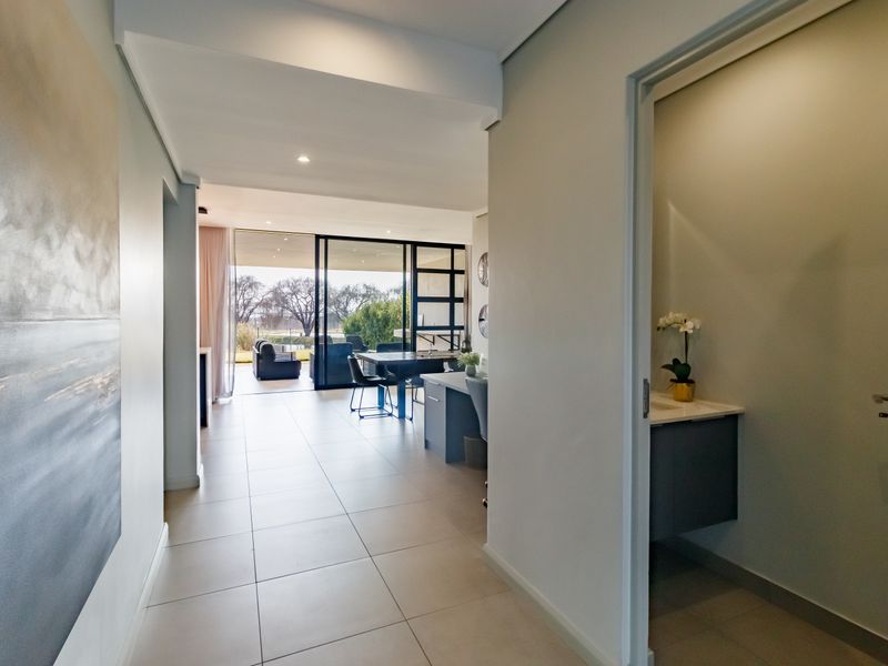 A bright hallway leading into an open-plan living area with large sliding glass doors, featuring a small adjacent vanity area.