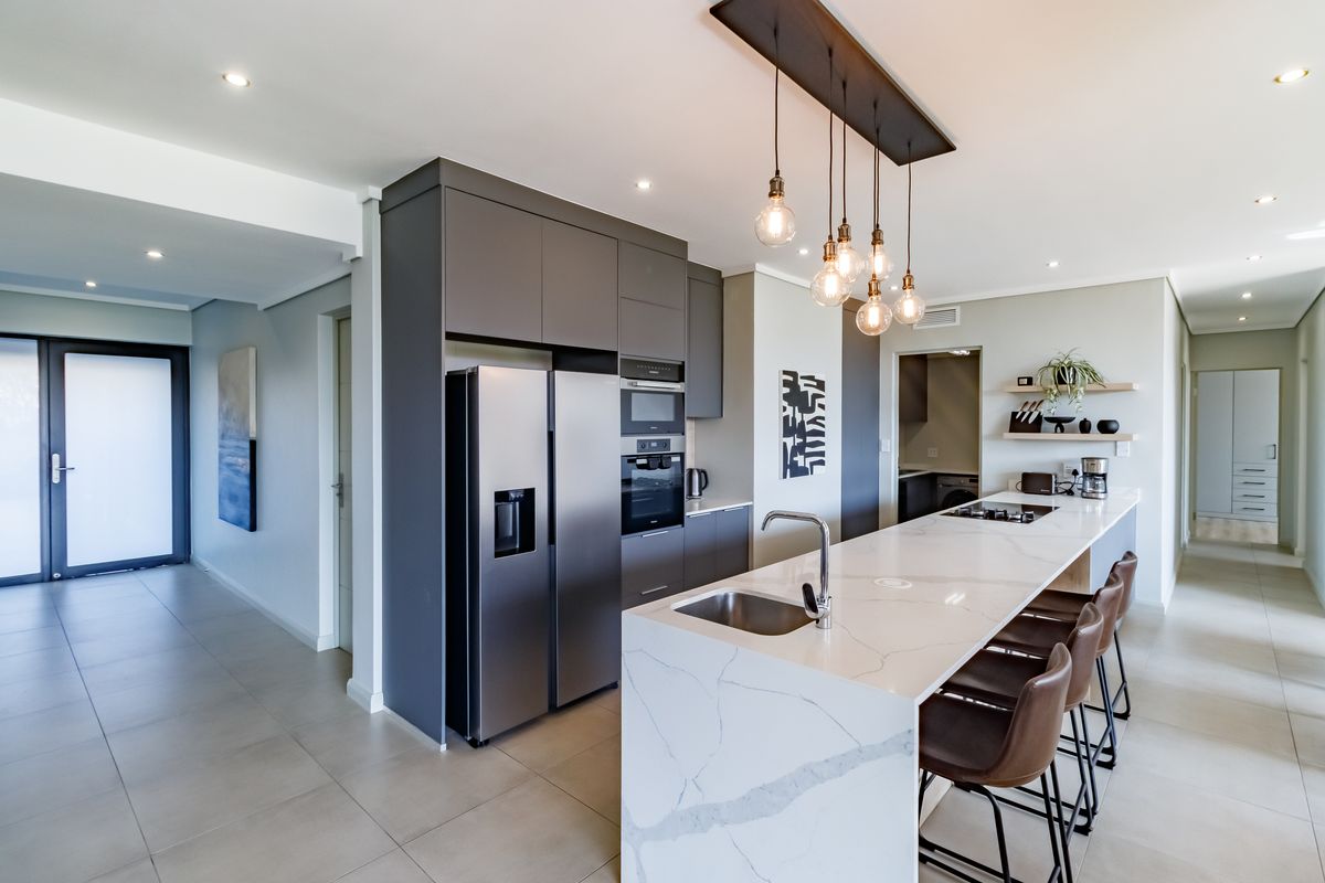Modern kitchen featuring a large quartz-topped island, integrated appliances, sleek dark cabinetry, and stylish pendant lighting in an open-plan layout.