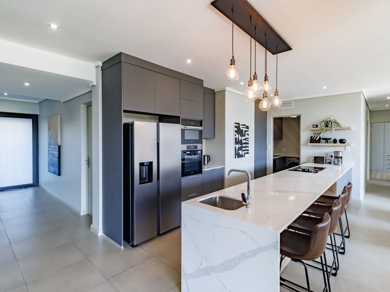 Modern kitchen featuring a large quartz-topped island, integrated appliances, sleek dark cabinetry, and stylish pendant lighting in an open-plan layout.