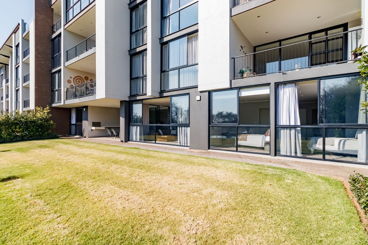 Rear view of a modern apartment building featuring ground floor patio access, large sliding glass doors, and a communal garden area.