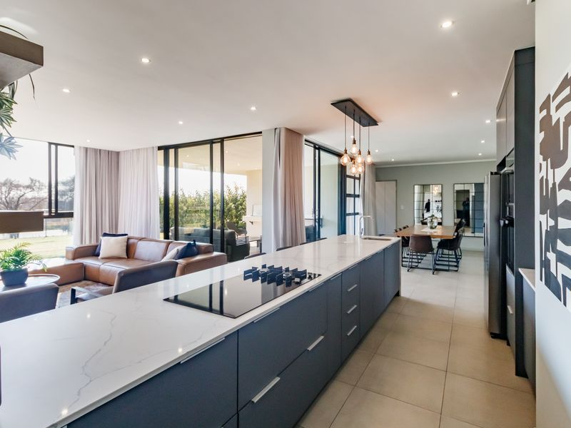 Modern open-plan living area featuring a sleek kitchen island with stone countertops, integrated hob, and seamless flow to the outdoor patio through sliding doors.