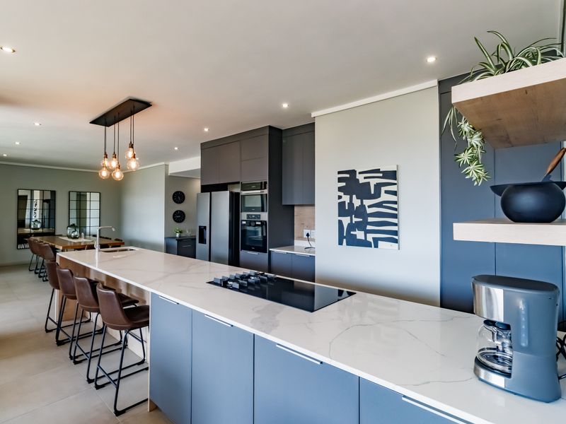 Modern open-plan kitchen and dining area featuring a large stone-topped island, built-in appliances, sleek cabinetry, and contemporary pendant lighting.