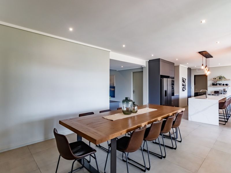 Modern open-plan living area featuring a sleek kitchen with a stone-topped island, recessed lighting, and neutral tiled flooring throughout.